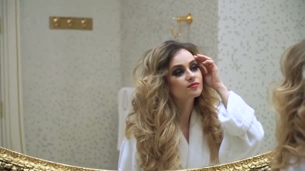 Piękna Blondynka koryguje jej włosy i patrząc w lustro w swojej łazience. Piękna młoda kobieta koryguje jej włosy. Fryzur — Wideo stockowe