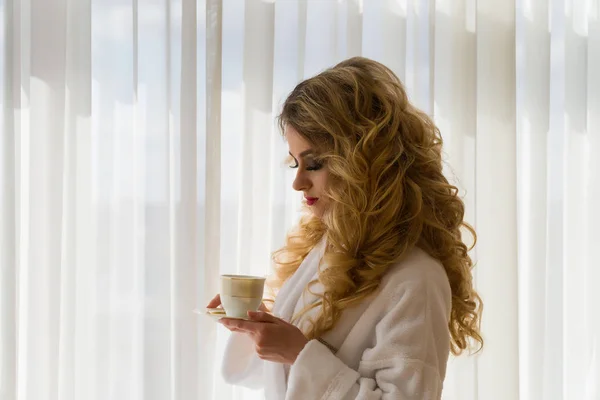 Schönheit Mädchen Kaffee trinken. schöne Frau öffnet Vorhänge, schaut aus dem Fenster und genießt ihren Morgenkaffee — Stockfoto