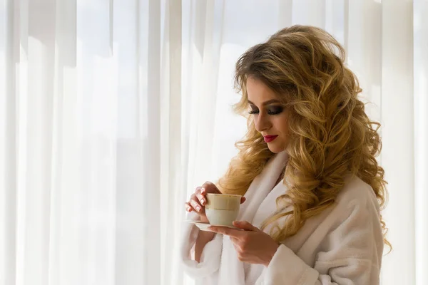 Schönheit Mädchen Kaffee trinken. schöne Frau öffnet Vorhänge, schaut aus dem Fenster und genießt ihren Morgenkaffee — Stockfoto