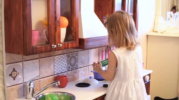 Active little preschool age child, cute toddler girl with blonde curly hair, shows playing kitchen, made of wood, plays in the kitchen — Stock Video