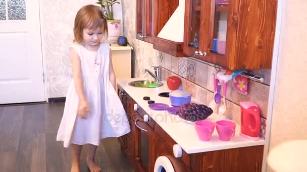 Active little preschool age child, cute toddler girl with blonde curly hair, shows playing kitchen, made of wood, plays in the kitchen — Stock Video