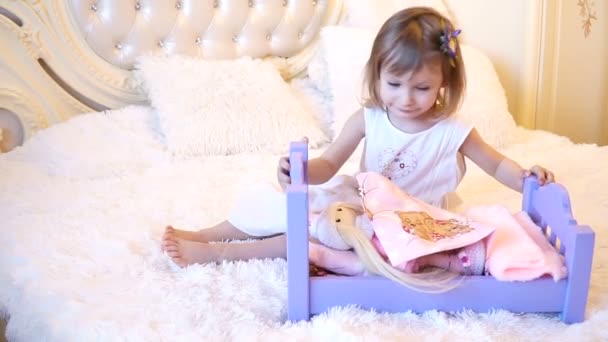 Ein aktives kleines Vorschulkind, ein hübsches kleines Mädchen mit blonden lockigen Haaren, spielt mit ihren Puppen, schläft sie ein — Stockvideo