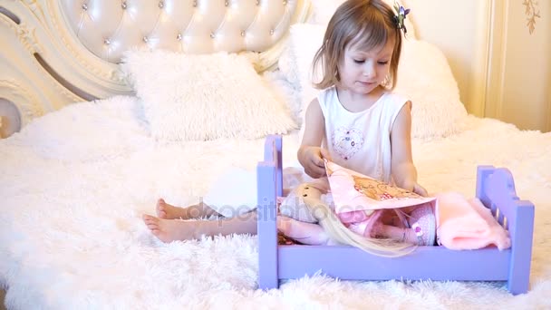 Un pequeño niño preescolar activo, una niña bonita con un pelo rubio rizado, juega con sus muñecas, las pone a dormir en — Vídeos de Stock