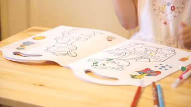 Kağıt renkli kalem ve keçeli kalemler, ahşap masa kapalı evde ya da anaokulu oturan kullanarak resim çizim etkin küçük okul öncesi yaş çocuk, sarı kıvırcık saçlı sevimli bebek kız