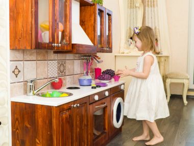 Aktif küçük okul öncesi yaş çocuk, şirin bebek kız sarışın kıvırcık saçlı, ahşap mutfak, oynarken gösterir çalış mutfakta