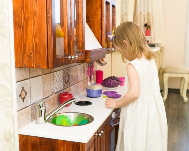 Aktif küçük okul öncesi yaş çocuk, şirin bebek kız sarışın kıvırcık saçlı, ahşap mutfak, oynarken gösterir çalış mutfakta