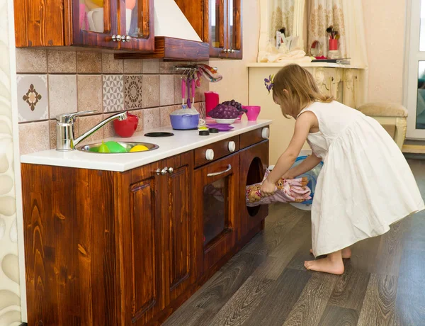 Ativo pequena criança em idade pré-escolar, menina bonito com cabelo encaracolado loira, mostra jogando cozinha, feita de madeira, joga na cozinha — Fotografia de Stock