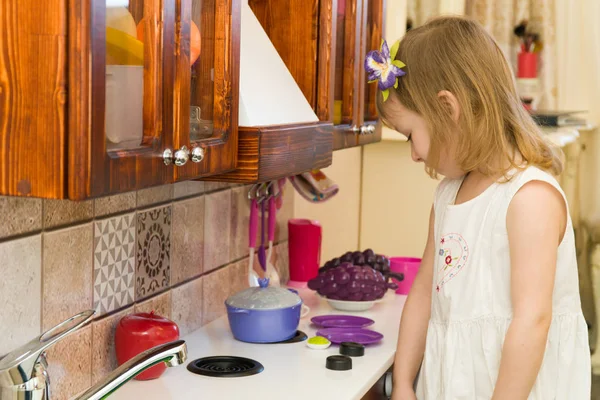 Pequeño niño en edad preescolar activo, linda niña con el pelo rubio rizado, muestra jugando cocina, hecha de madera, juega en la cocina — Foto de Stock