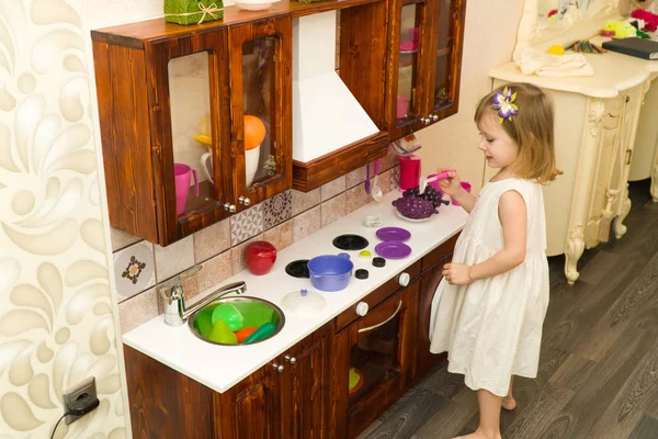 Pequeño niño en edad preescolar activo, linda niña con el pelo rubio rizado, muestra jugando cocina, hecha de madera, juega en la cocina — Foto de Stock