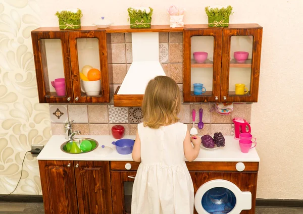 Aktives kleines Kind im Vorschulalter, niedliches Kleinkind mit blonden Locken, zeigt Spielküche, aus Holz, spielt in der Küche — Stockfoto