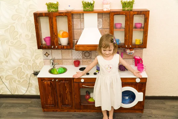 Ativo pequena criança em idade pré-escolar, menina bonito com cabelo encaracolado loira, mostra jogando cozinha, feita de madeira, joga na cozinha — Fotografia de Stock