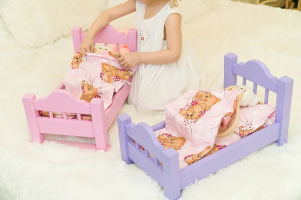 Uma criança pré-escolar ativa, uma menina bonita com um cabelo encaracolado loiro, brinca com suas bonecas, as coloca para dormir em um roubo — Fotografia de Stock