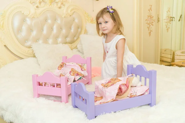 Een actieve preschool kindje, een mooi klein meisje met een blond krullend haar, speelt met haar poppen, zet ze om te slapen in een te stelen — Stockfoto