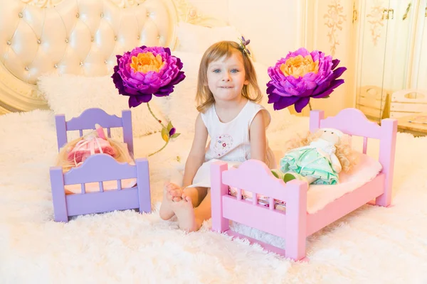 Uma criança pré-escolar ativa, uma menina bonita com um cabelo encaracolado loiro, brinca com suas bonecas, as coloca para dormir em um roubo — Fotografia de Stock