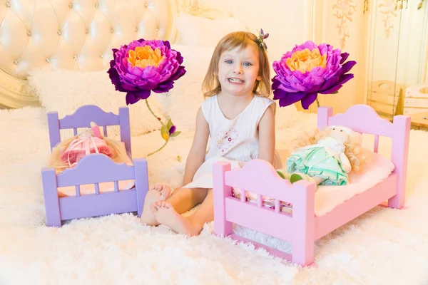 Uma criança pré-escolar ativa, uma menina bonita com um cabelo encaracolado loiro, brinca com suas bonecas, as coloca para dormir em um roubo — Fotografia de Stock