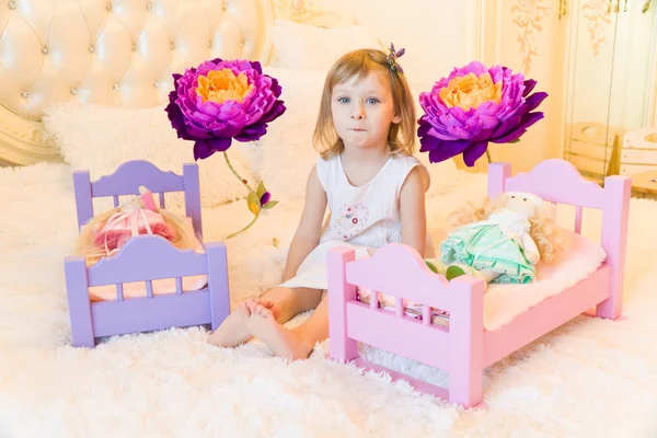 Uma criança pré-escolar ativa, uma menina bonita com um cabelo encaracolado loiro, brinca com suas bonecas, as coloca para dormir em um roubo — Fotografia de Stock