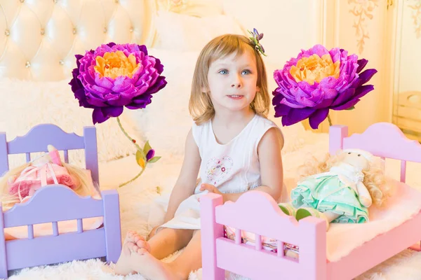 Uma criança pré-escolar ativa, uma menina bonita com um cabelo encaracolado loiro, brinca com suas bonecas, as coloca para dormir em um roubo — Fotografia de Stock