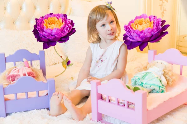 Uma criança pré-escolar ativa, uma menina bonita com um cabelo encaracolado loiro, brinca com suas bonecas, as coloca para dormir em um roubo — Fotografia de Stock