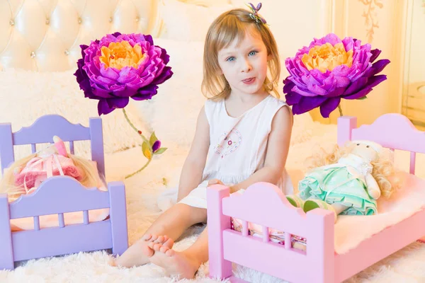 Uma criança pré-escolar ativa, uma menina bonita com um cabelo encaracolado loiro, brinca com suas bonecas, as coloca para dormir em um roubo — Fotografia de Stock