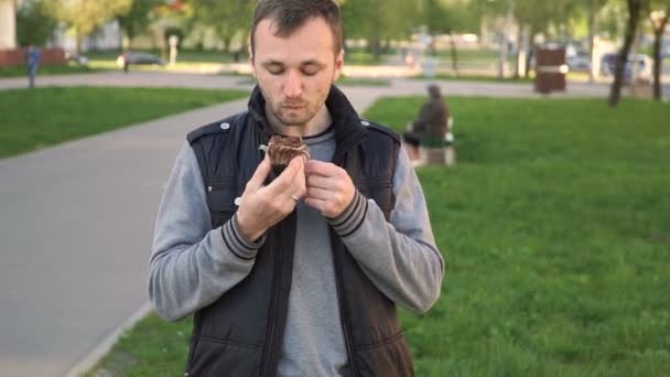 Zoet voedsel en mensen concept. jonge man eten chocolade taart in het park — Stockvideo