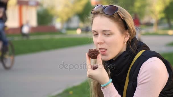 Zoet voedsel en mensen concept. jonge wooman eten chocolade taart in het park en grappig bijten het. — Stockvideo