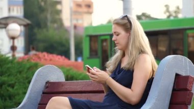Şehir parkında bir bankta oturan akıllı telefonu kullanan mutlu kız.