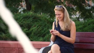 Havuzun yanındaki bir bankta oturmuş bir şehir parkta bir akıllı telefon kullanan mutlu kız