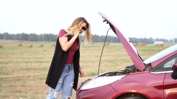 Blondes Mädchen telefoniert in Panik in der Nähe ihres kaputten Autos mit offener Motorhaube auf einer Landstraße — Stockvideo