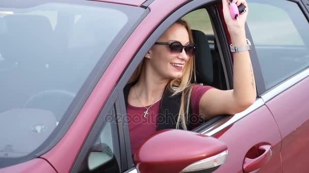 Jovem mulher feliz atraente senta-se no carro e mostra a chave do novo carro - absolutamente satisfeito — Vídeo de Stock