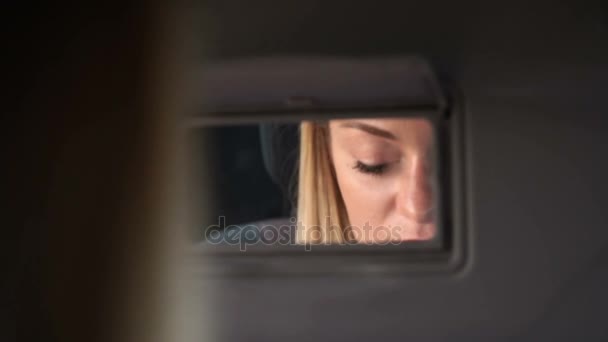 Νεαρή ξανθιά γυναίκα χρωματίζει τα χείλη της στο αυτοκίνητο. Ο ήλιος φωτίζει το πρόσωπο. Κοντινό πλάνο. — Αρχείο Βίντεο