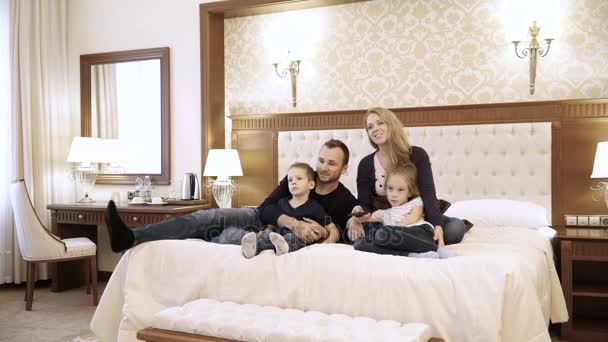 Щаслива сім'я, що дивиться телевізор у готельному номері, що сидить на ліжку — стокове відео