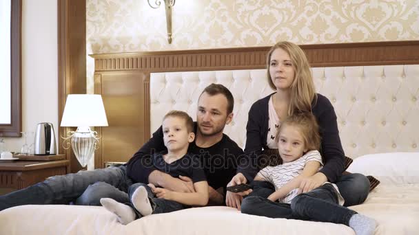 Una familia feliz viendo la televisión en la habitación del hotel sentado en la cama — Vídeos de Stock