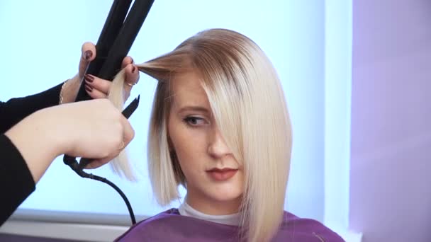 Парикмахер сглаживает волосы красивой молодой девушки. выпрямление волос — стоковое видео