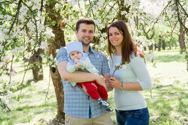 Jeune famille heureuse marchant en plein air. Les parents tiennent l'enfant sur les mains et se réjouissent. Ils sont heureux ensemble. Souriez-vous. — Photo