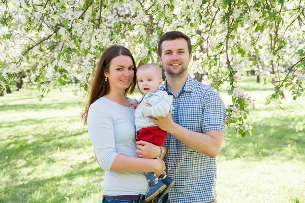 Jeune famille heureuse marchant en plein air. Les parents tiennent l'enfant sur les mains et se réjouissent. Ils sont heureux ensemble. Souriez-vous. — Photo