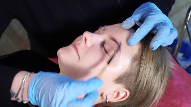 Esteticista, especialista en maquillaje permanente está aplicando anestésico local antes del procedimiento de maquillaje permanente de las cejas. primer plano . — Vídeo de stock