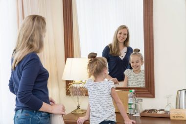 Genç anne ve kızı bir otel odasında bir ayna önünde duran ve gülümseyerek. Aile çok mutlu