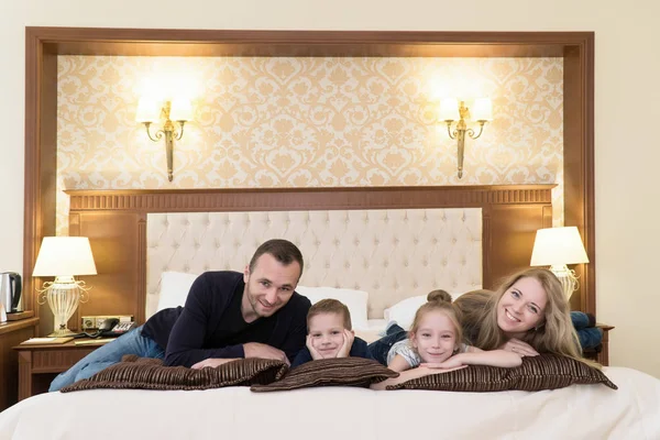 Una famiglia felice posa sulla macchina fotografica in camera d'albergo seduta sul letto Foto Stock Royalty Free