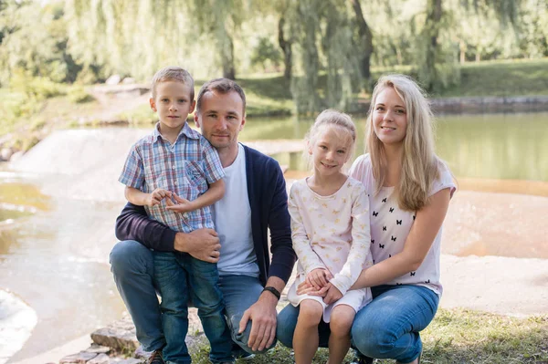 Mama und Papa spielen mit ihrem hübschen Sohn und ihrer Tochter - Familie und Kinder draußen im Park - junge schöne Familie posiert für den Fotografen Stockbild