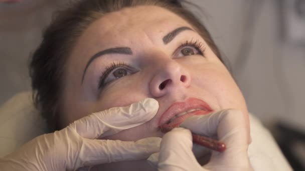 Um tiro de perto. Especialista profissional em maquiagem permanente aplicando lábios antes do procedimento. Conceito de beleza, maquiagem e moda — Vídeo de Stock