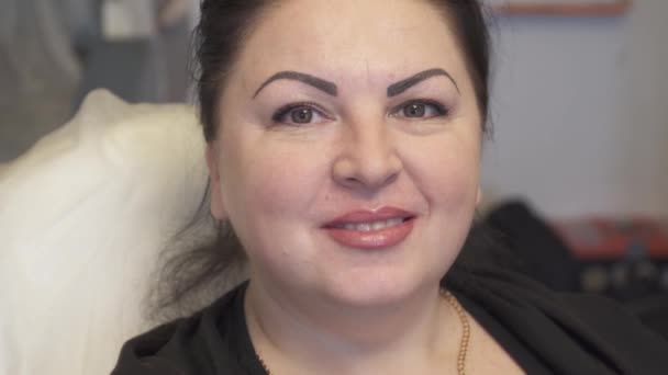 Kvinna brunett med långt hår ser ut i spegeln efter den permanent make-up, lycklig, leende — Stockvideo