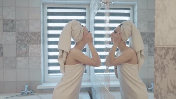 Jeune, jolie femme avec une serviette sur la tête et le corps peint ses yeux dans la salle de bain. Concept beauté et maquillage — Video