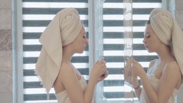 Bella donna con asciugamano in testa e corpo applicando crema per la cura della pelle al viso. Concetto bellezza — Video Stock