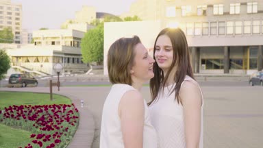 Anne ve gülüyor ve güneşli bir günde parkta sohbet yetişkin kızı. Her anne sarılma sevgi ve hassasiyet ile çekici esmer olduğunu
