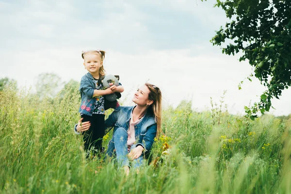 Jovem mãe com filha na natureza entre a grama verde — Fotografia de Stock