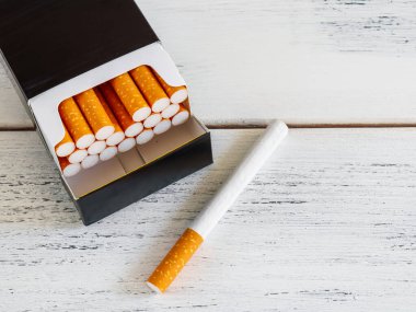 Sigaralar beyaz ahşap bir masanın üzerinde siyah bir deste içinde. Üst görünüm, kapat.