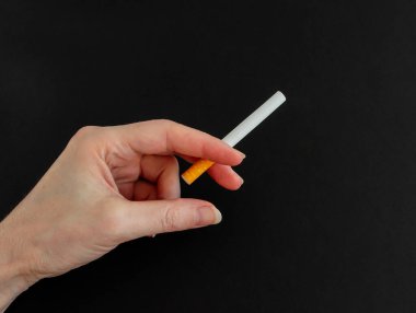 Kadın eli siyah arka planda sigara tutuyor. Yakın çekim, sol..