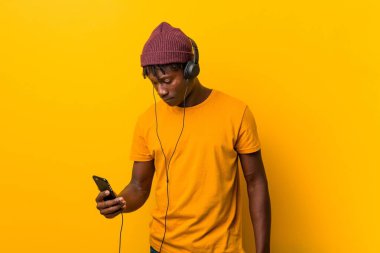 Bir telefon ile müzik dinlerken bir şapka giyen sarı bir arka plan karşı duran genç Afrikalı adam