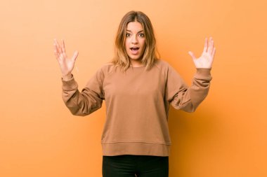 Hoş bir sürpriz alan bir duvara karşı genç otantik karizmatik gerçek insanlar kadın, heyecanlı ve ellerini yükselterek.