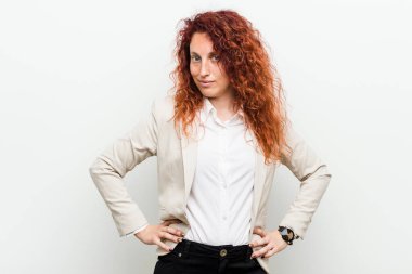 Genç, kızıl saçlı iş kadını, beyaz arka planda izole edilmiş, kendine güveni tam, kalçalarını tutuyor..